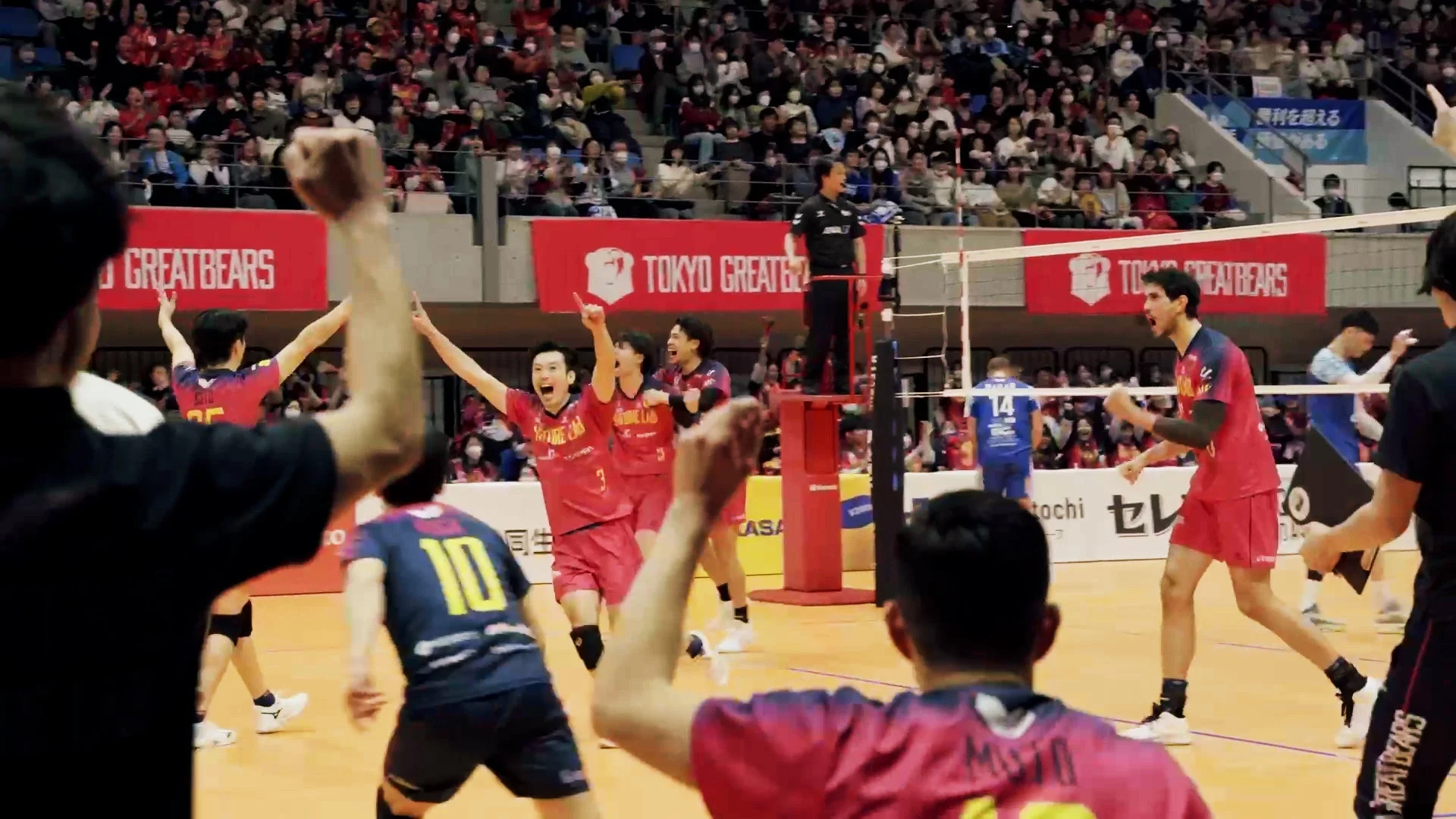バレーボールの試合で、赤いユニフォームの選手たちが得点を決めて喜びを爆発させている瞬間
