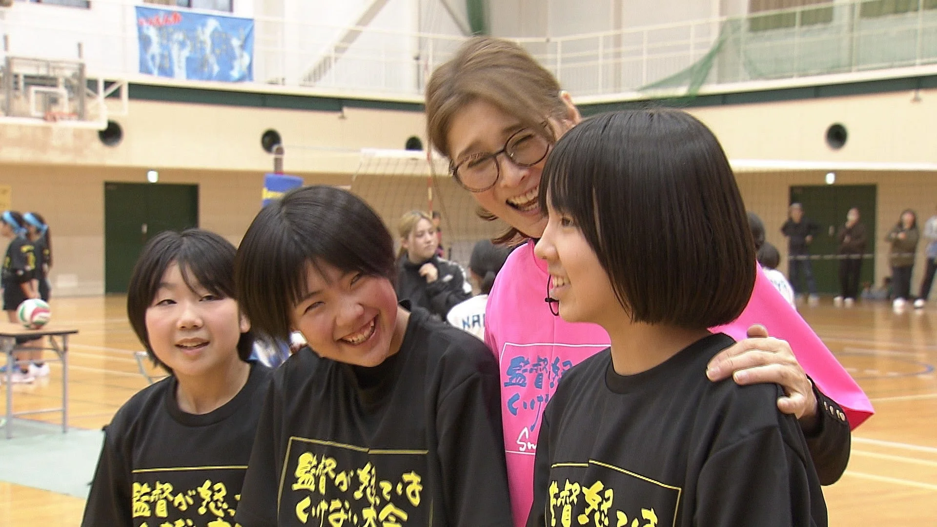 体育館で笑顔の女性コーチが3人の若い女子選手たちと交流している様子