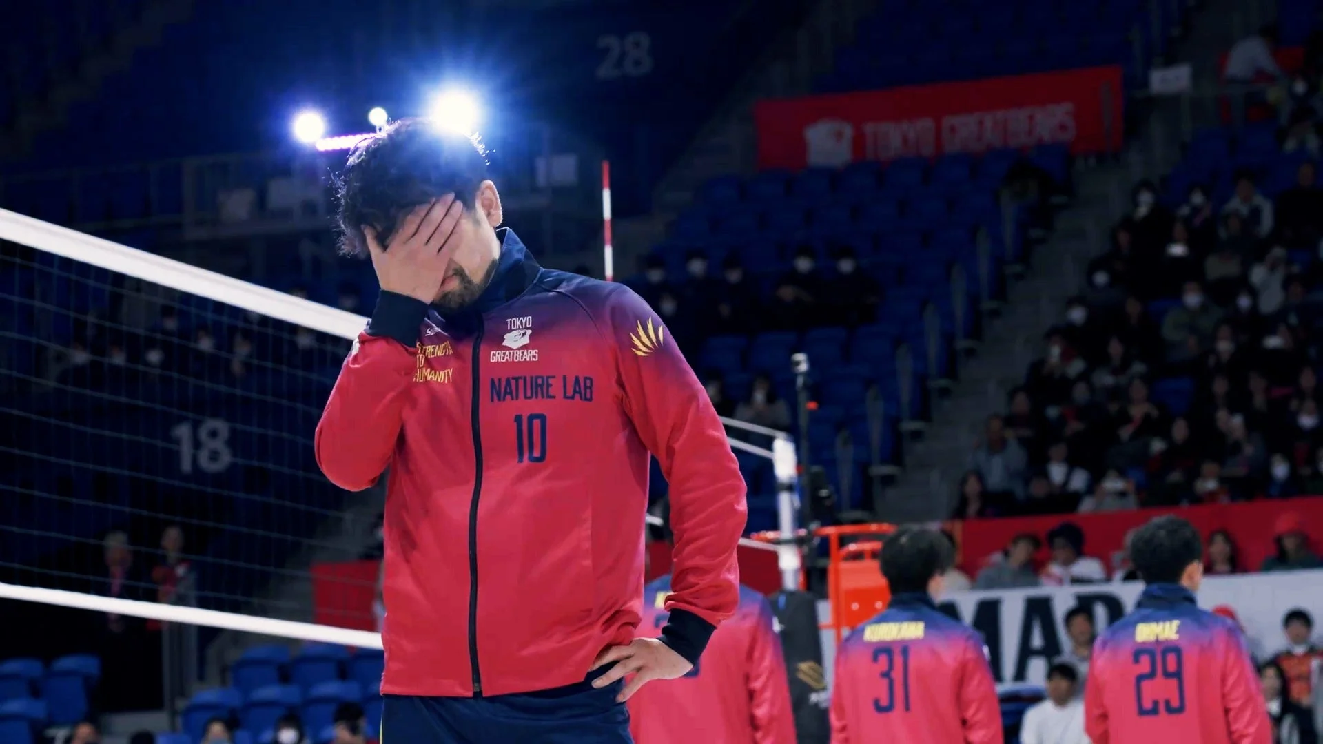 バレーボールの試合中に、赤いユニフォームを着た選手が顔を覆い、悔しさや疲労を表している様子