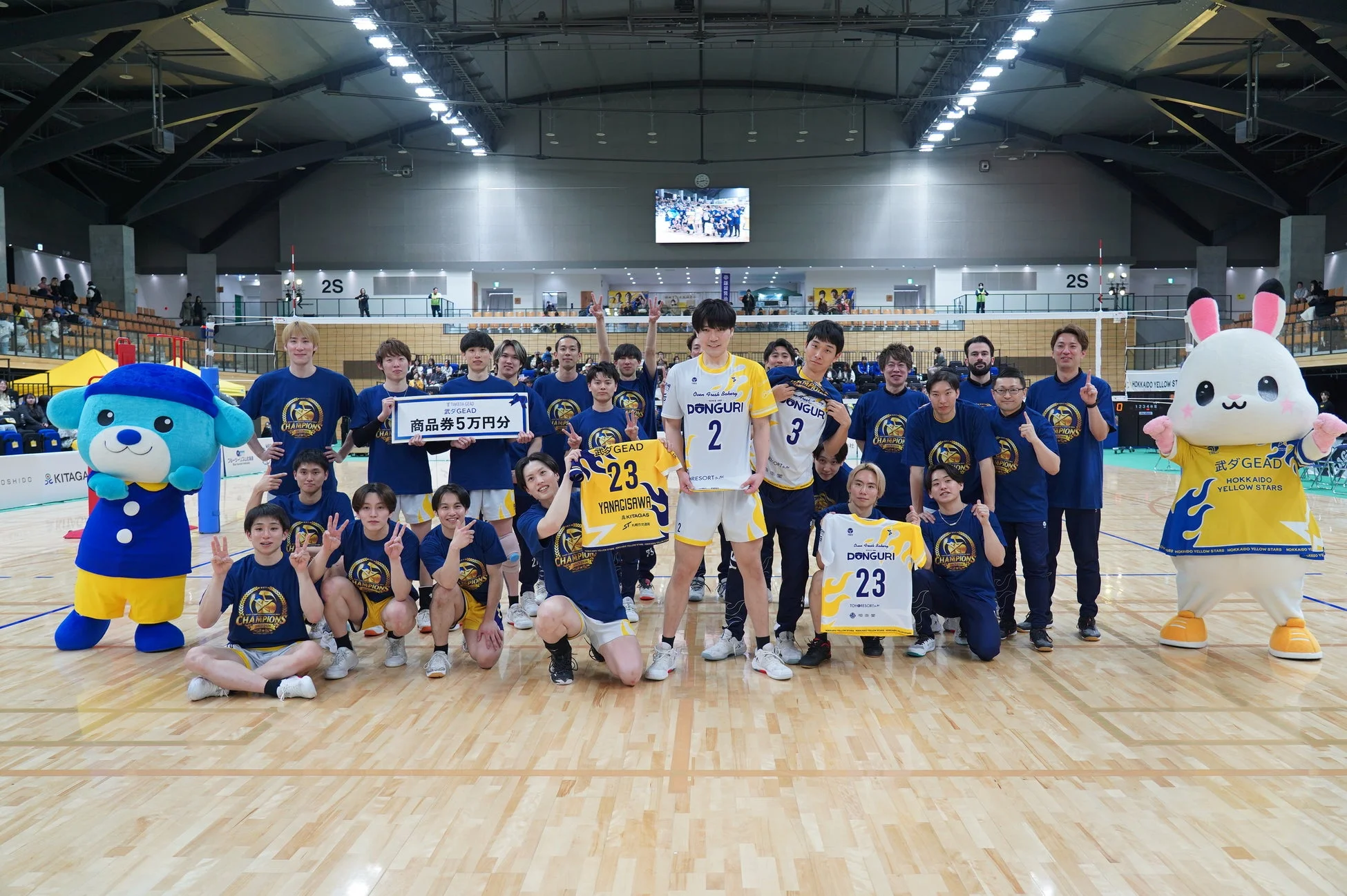 体育館のバレーボールコートで、ユニフォーム姿の選手たちが集合写真を撮っています。