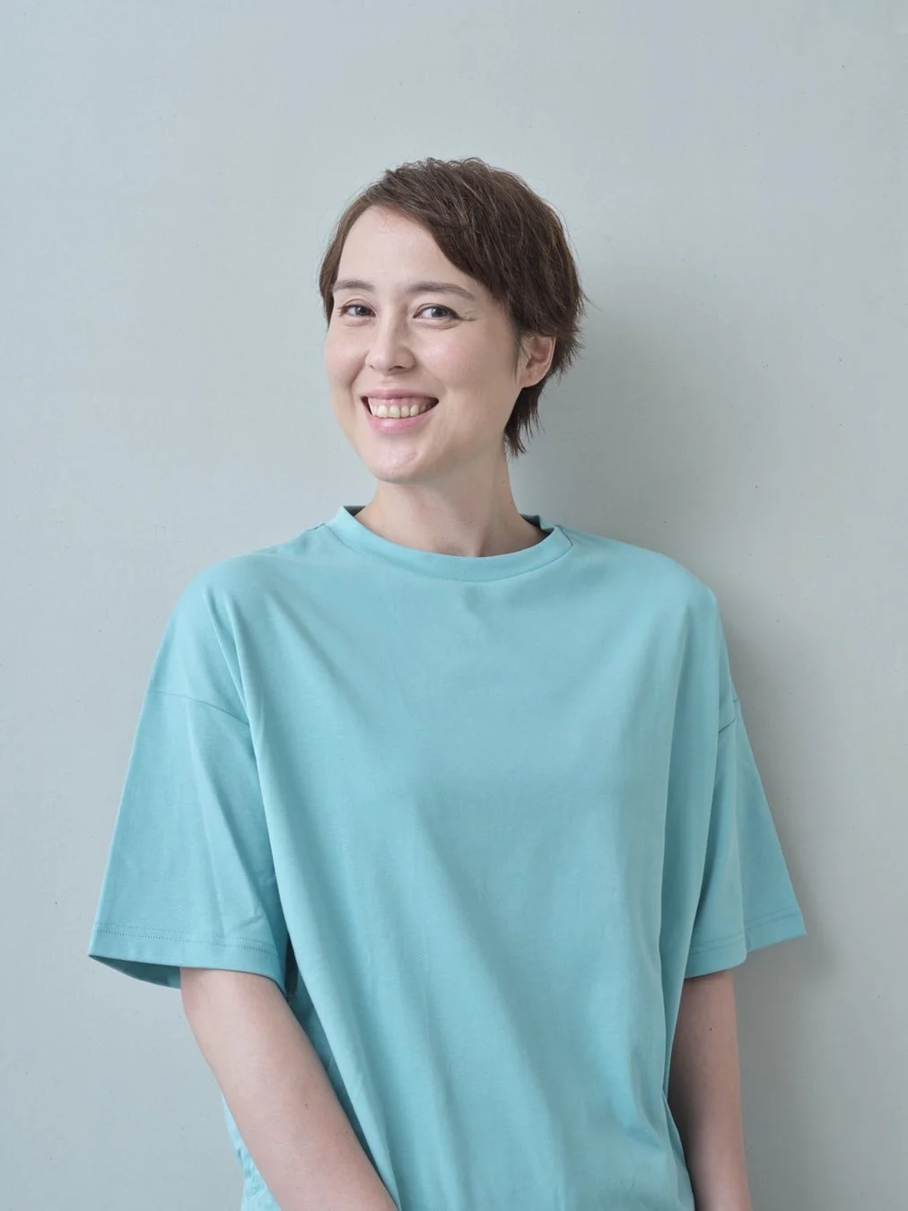 水色のTシャツを着て、ショートヘアの女性が満面の笑みを浮かべているポートレート写真