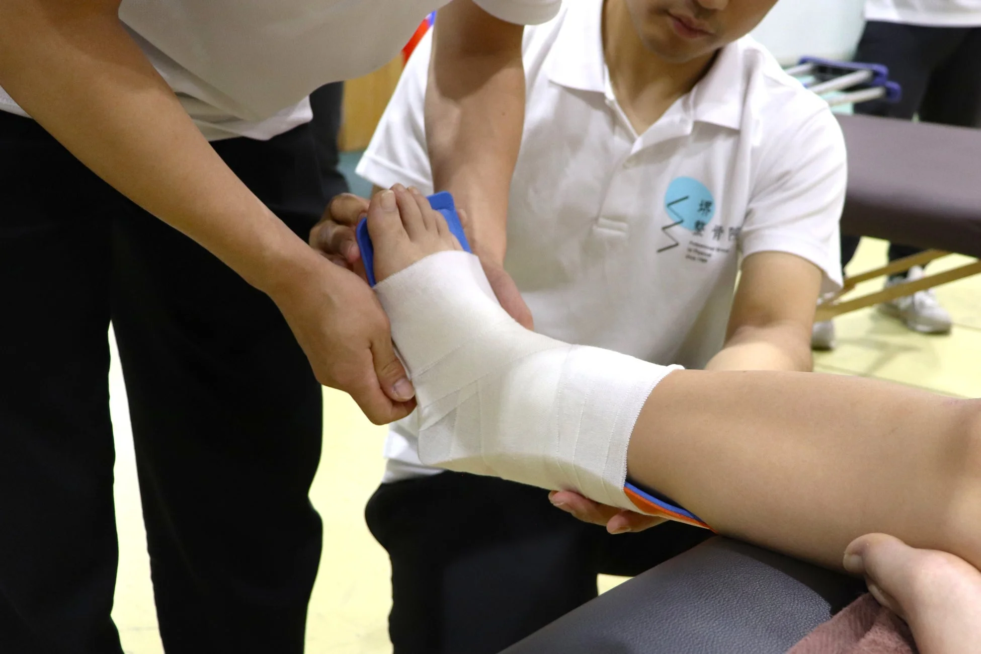 整骨院で、専門家が患者の足首に白いテーピングを施している様子