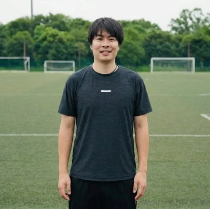 サッカー場のような緑のグラウンドに立つ若い男性のポートレート