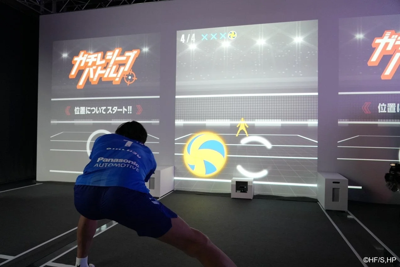 一人の人物が大きなスクリーンに投影されたバレーボールのインタラクティブゲームをプレイしている様子です。プレイヤーはPanasonic AUTOMOTIVEのシャツを着ており、臨場感あふれるスポーツ体験をしているようです。