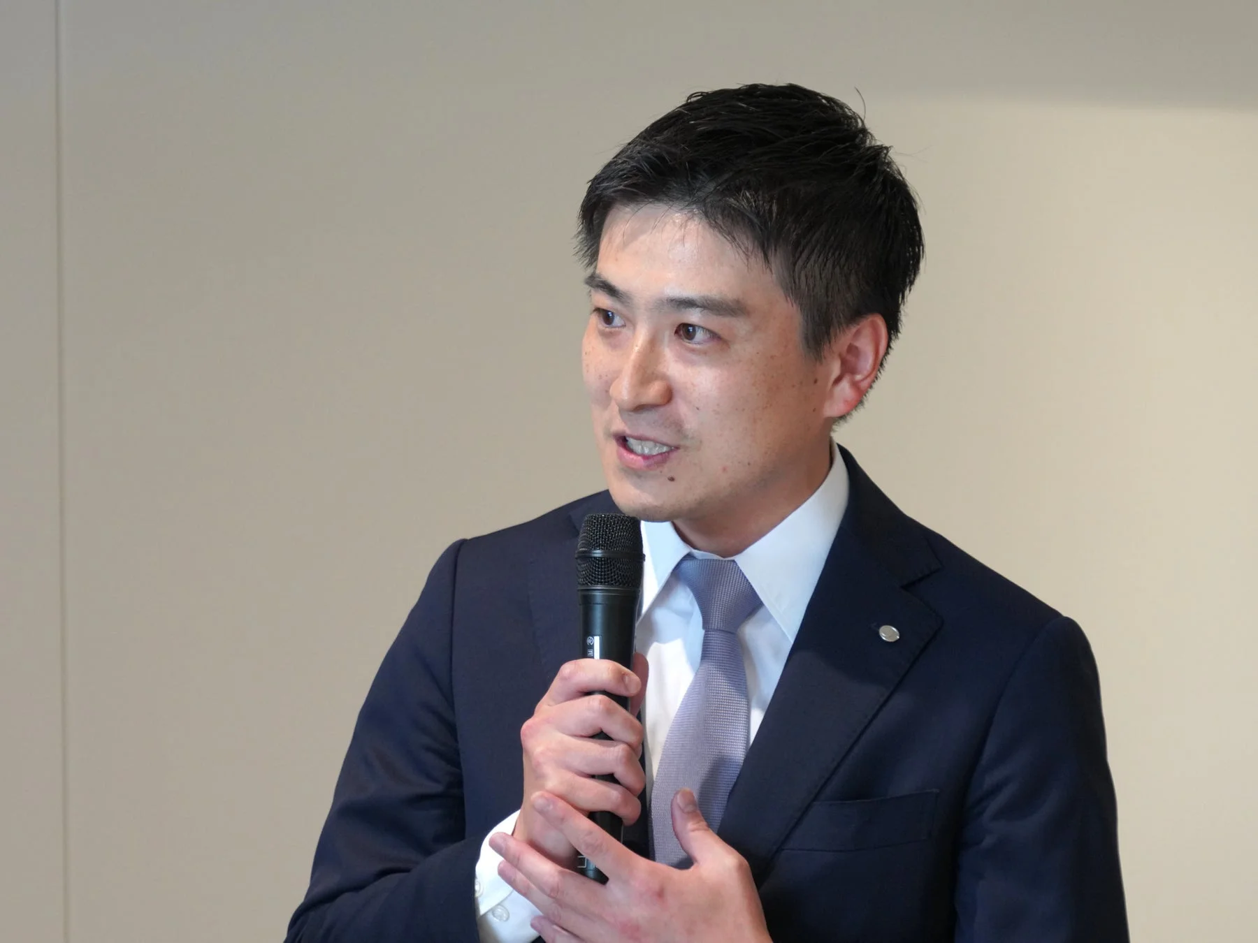 スーツを着た男性がマイクを持ち、熱心に話している様子