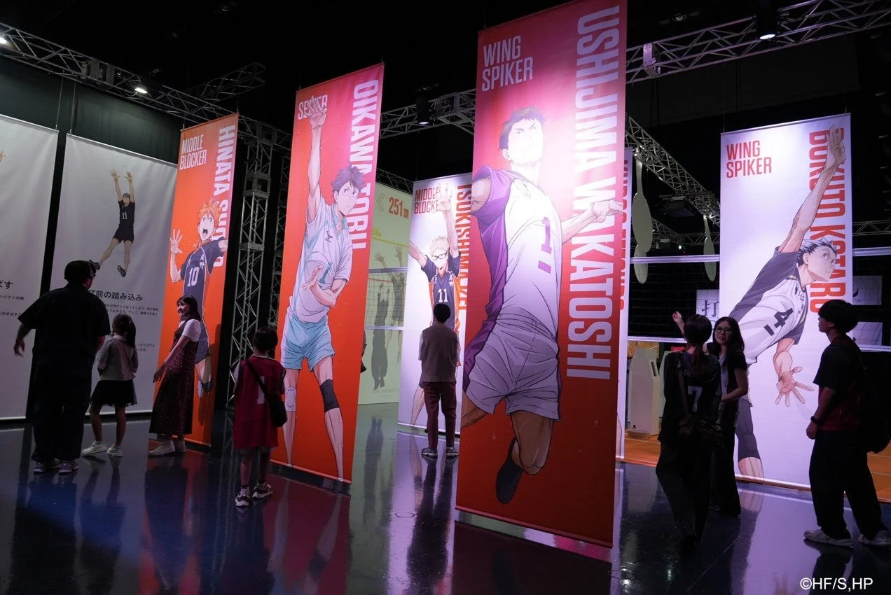 人気バレーボールアニメ「ハイキュー!!」のキャラクターが描かれた巨大なバナーが並ぶ展示会場の様子です。来場者がそれぞれのキャラクターイラストを鑑賞しており、アニメの世界観が感じられるイベント空間となっています。