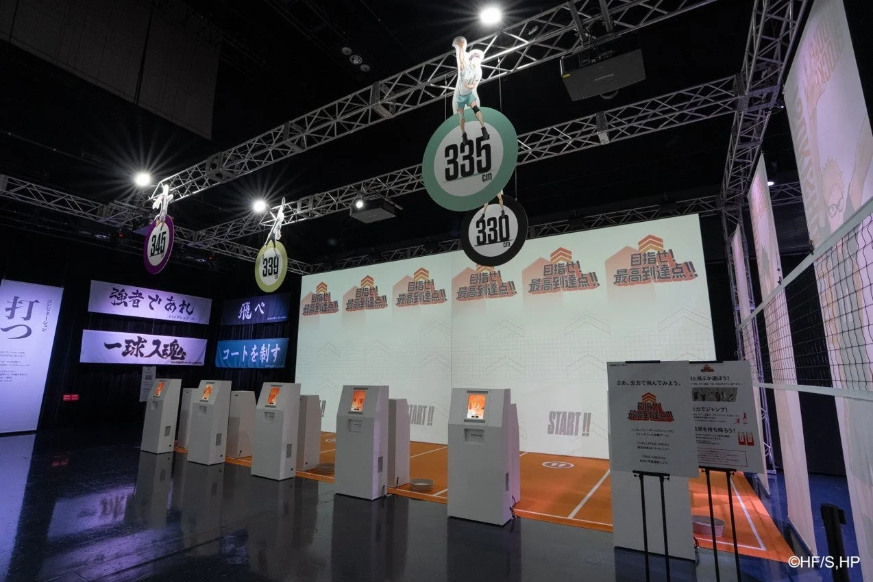 人気アニメ「ハイキュー!!」のイベント会場で、バレーボールの最高到達点に挑戦する体験型アトラクションの様子。キャラクターのパネルや目標となる高さが示され、参加者がジャンプ力を試せる楽しい空間が広がっている。