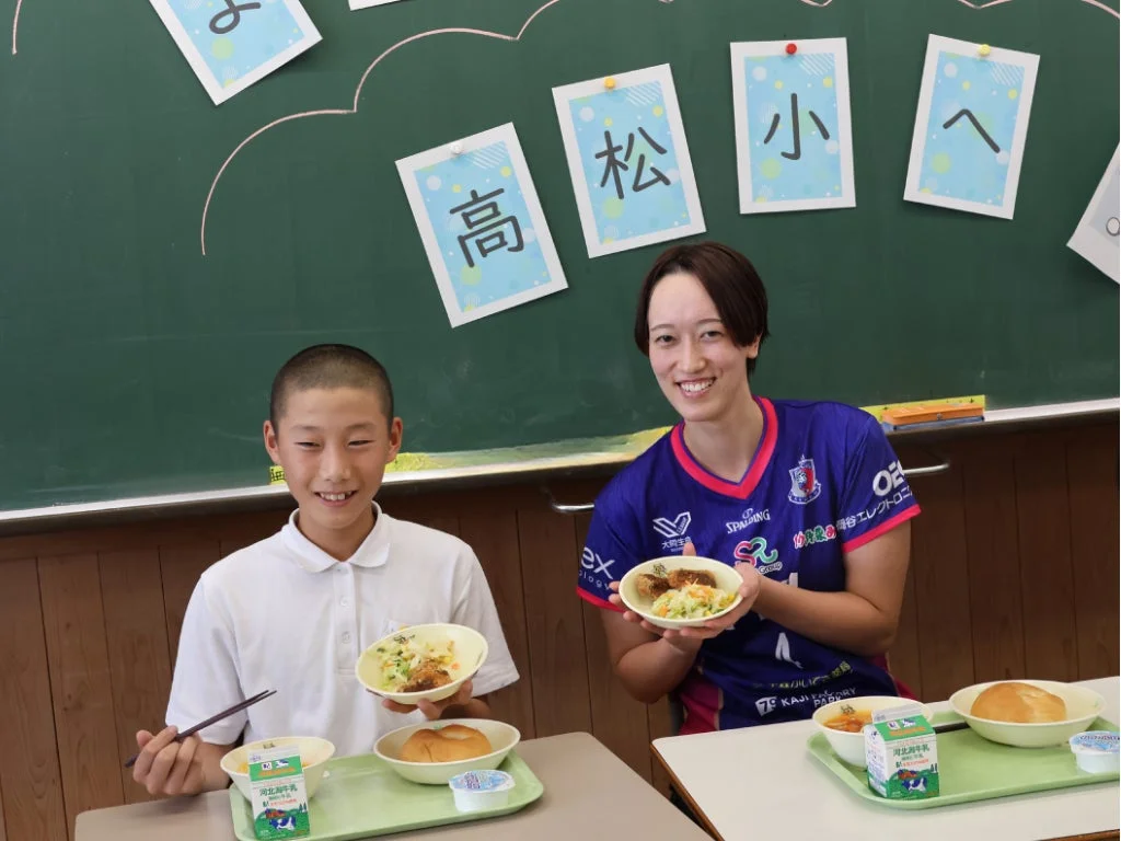 教室で給食を食べる選手と生徒